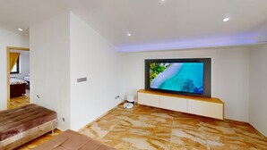 Ein modernes Wohnzimmer mit einem großen Flachbildfernseher, der an einem Holzschrank befestigt ist, einem braunen Sofa und einem gemusterten Boden.