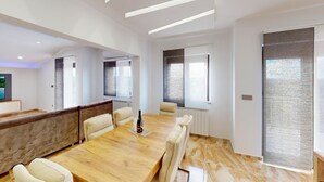 Ein moderner Konferenzraum mit einem Holztisch, beigen Stühlen und einem großen Fenster mit Jalousien.