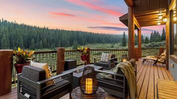 Relax on the deck with scenic views of the surrounding forest, featuring a sofa, chair, and table with a lamp.