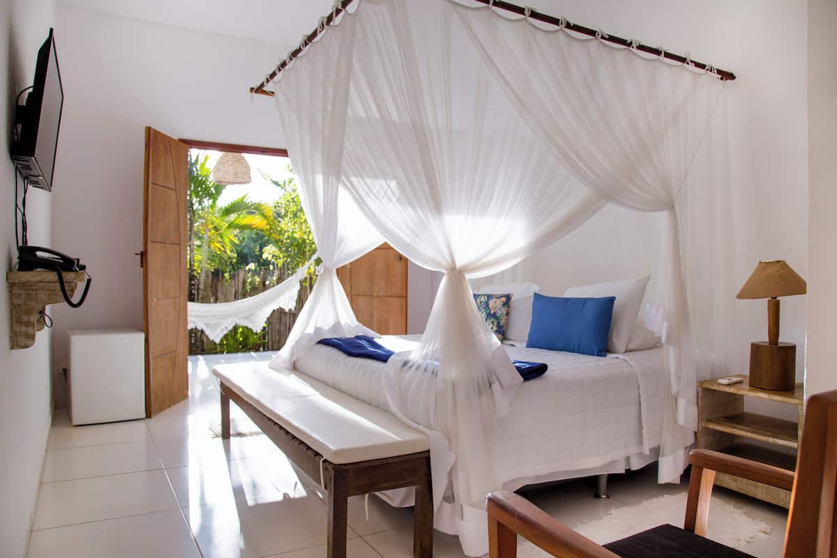 A bedroom with a canopy bed, a bench, a bedside table, and a lamp.