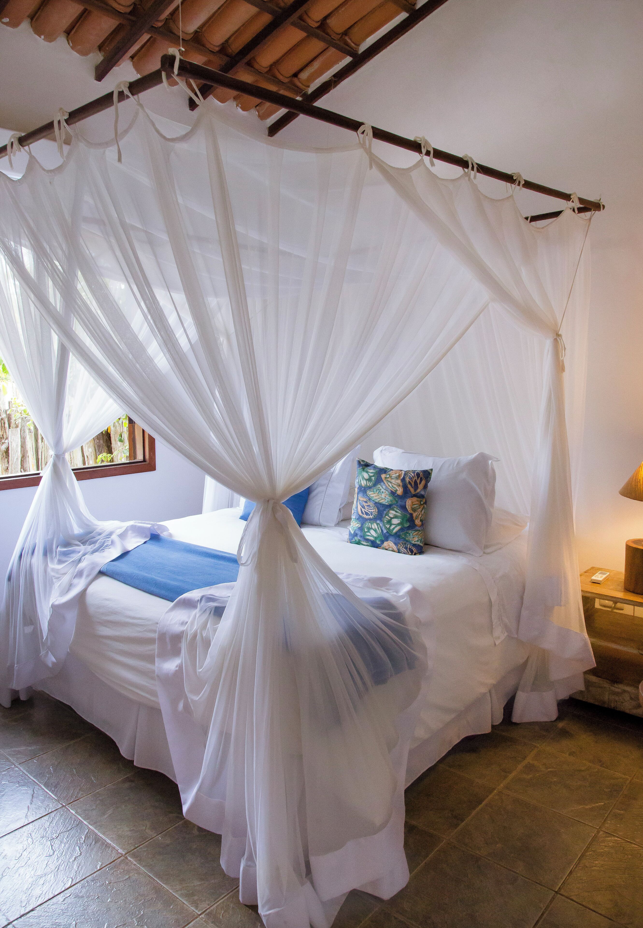 A bed with a white canopy, a blue pillow, and a wooden nightstand with a lamp.