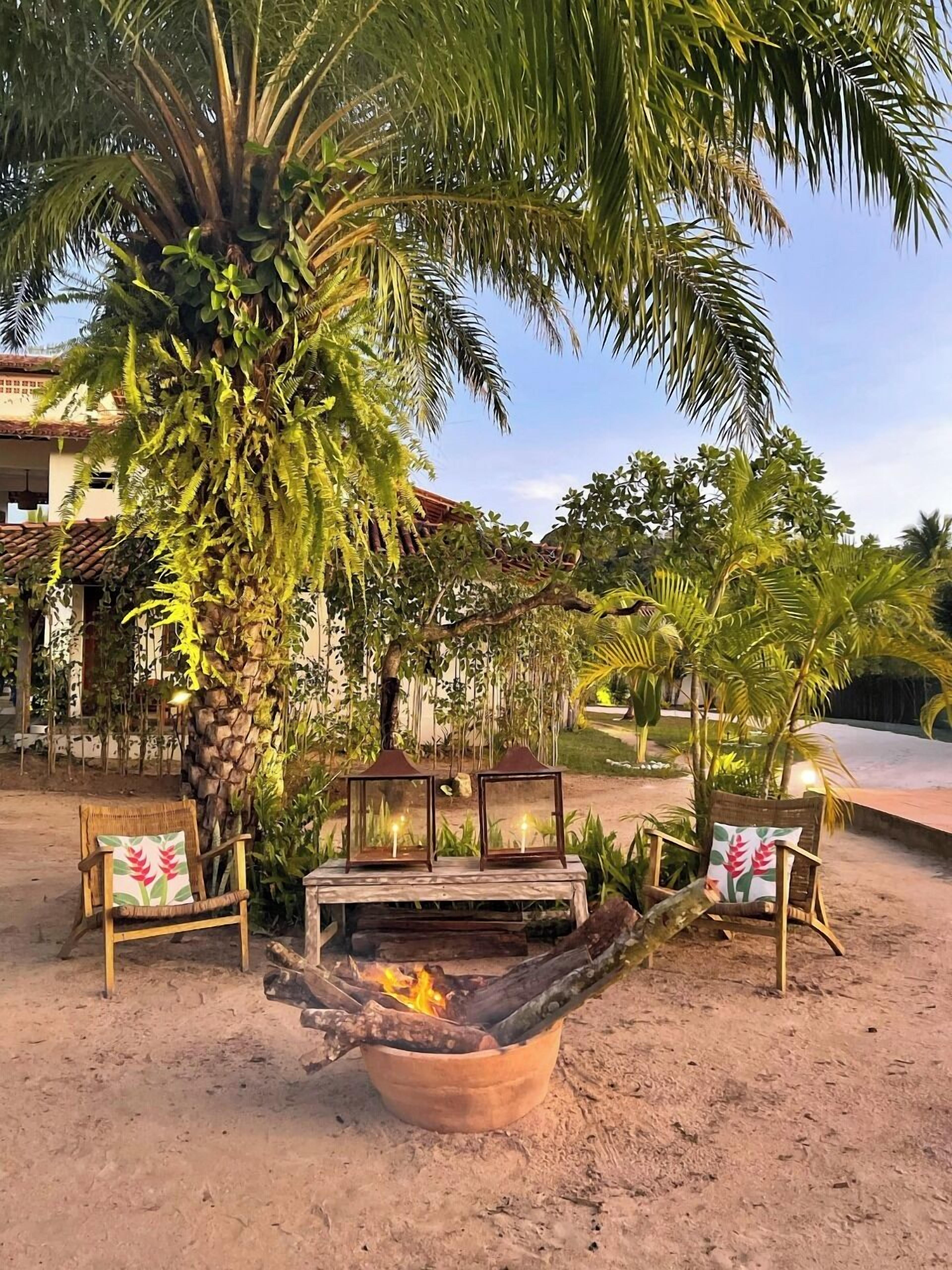 An outdoor seating area with a fire pit, two chairs with cushions, and a wooden table.