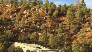 Un bâtiment moderne doté d’un toit plat et de grandes fenêtres, entouré d’un paysage naturel composé d’arbres et de reliefs rocheux.