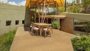 Une terrasse extérieure moderne, dotée d’une table et de chaises en bois, entourée d’un sol en béton et protégée par une paroi en verre.