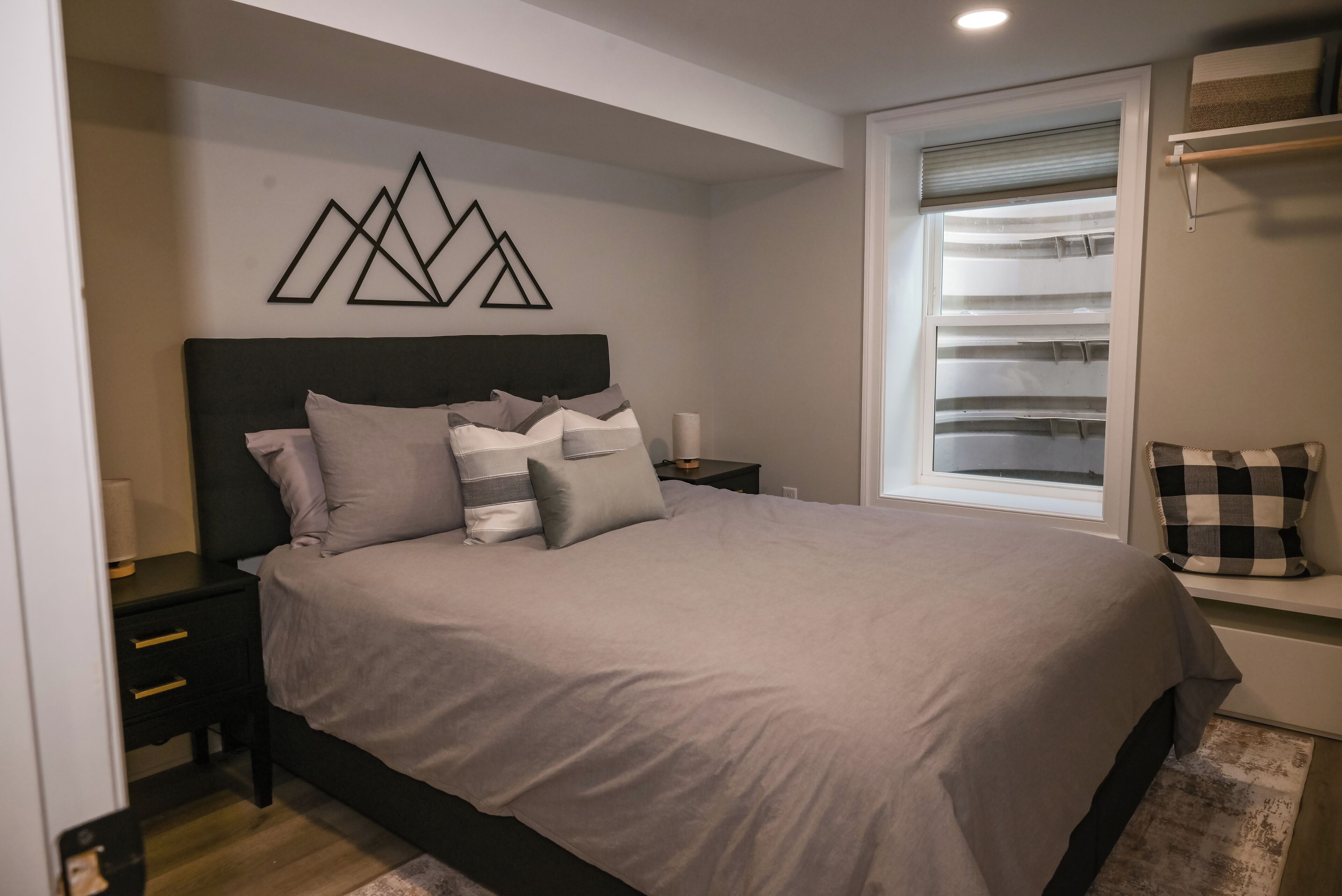 A bedroom with a bed, nightstands, a window with blinds, and a wall-mounted geometric decoration.
