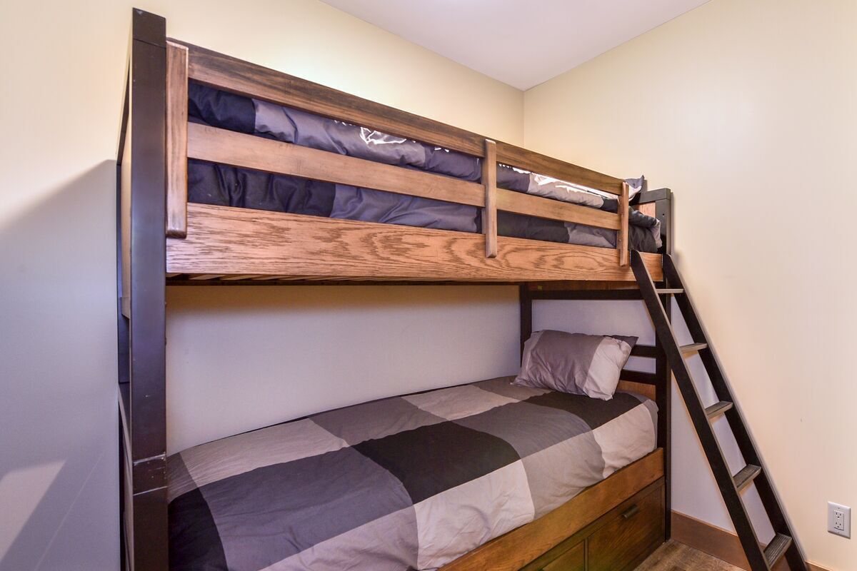 Un letto a castello con una scala in legno e un letto inferiore con coperta a quadretti.