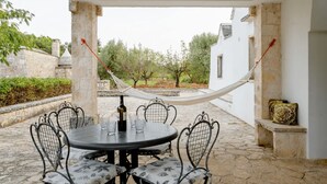 A covered outdoor dining area with a round table, chairs, and a hammock.