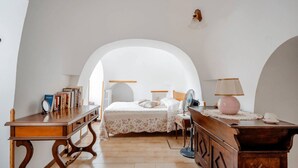 A bedroom with a bed, a desk, a dresser, and a fan.