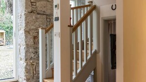 A staircase with wooden railings leading to a second floor, a stone wall, and a view of the outdoors.