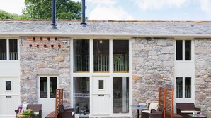 A stone building with a large glass door, outdoor seating area with wicker furniture, and a chimney. - Tack Room a luxury Poldark retreat (Camborne)