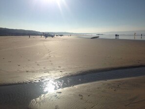 A wide sandy beach with footprints and a calm sea.