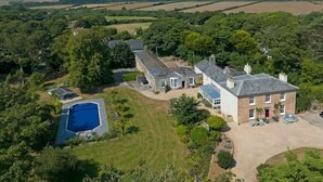 Una casa grande con piscina, rodeada de exuberante follaje y campos.