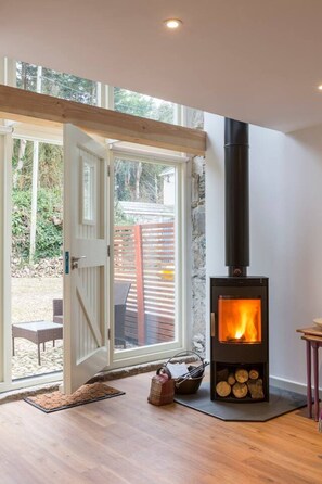 A room with a wood-burning stove, a sliding glass door leading to an outdoor area, and a small table with a chair.