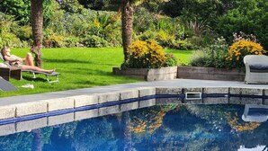 Una piscina con superficie de agua cristalina y azul, rodeada por un jardín bien cuidado con diversas plantas y flores.