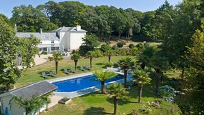 A pool surrounded by palm trees and a white building with a glass conservatory. - Tack Room a luxury Poldark retreat (Camborne)