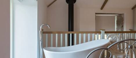 A modern bathroom with a freestanding bathtub, a window, and a wooden ceiling beam.