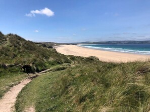 A coastal path leading to a sandy beach with a clear sky.