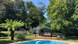 Una piscina con cubierta de madera, rodeada de abundante vegetación y un pequeño cobertizo.