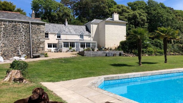 Un patio trasero con piscina, un perro tumbado en la terraza y un edificio de piedra.
