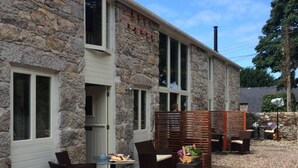 A stone building with a patio area featuring wicker furniture and a table with food. - The Hayloft - A Romantic Boutique Retreat (Camborne)