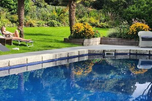 A swimming pool with a clear blue water surface, surrounded by a well-maintained garden with various plants and flowers.