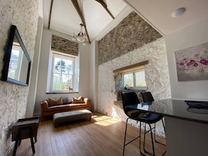 A room with a stone wall, a wooden ceiling, a sofa, a dining table, and a chair. - Bramble’s Cottage (Cornwall)