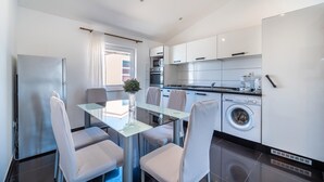 Una cucina moderna con zona pranzo, comprensiva di tavolo in vetro, sedie, frigorifero, forno, microonde e lavatrice.