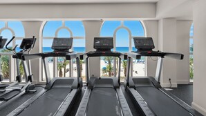 A gym with treadmills and exercise equipment, large windows with a beach view.