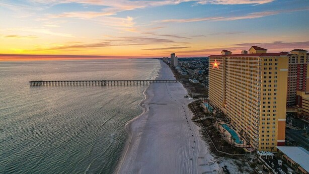 A coastal hotel with a long pier extending into the sea, adjacent to a sandy beach.