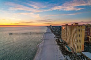A coastal hotel with a long pier extending into the sea, adjacent to a sandy beach.