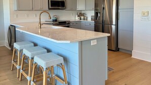 A modern kitchen with grey cabinets, stainless steel appliances, a central island with bar stools, and a wooden floor. - 1 MINUTUE WALK TO BEACH FROM BHI BEACH FRONT HOME (Bald Head Island)