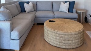 A modern living room with a grey sectional sofa, a round woven ottoman, and a ceiling fan. - 1 MINUTUE WALK TO BEACH FROM BHI BEACH FRONT HOME (Bald Head Island)