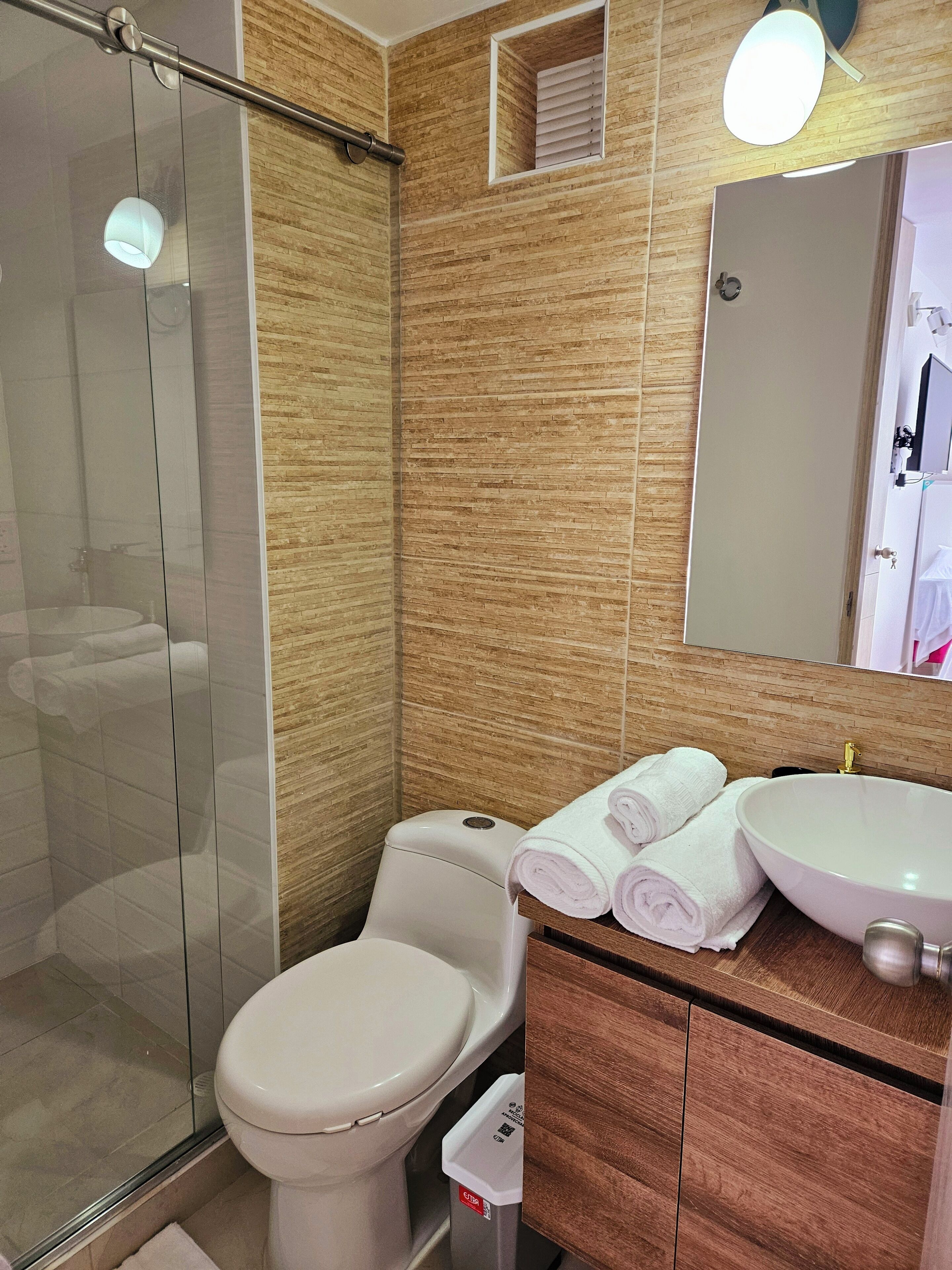 Ein modernes Badezimmer mit Duschkabine aus Glas, Toilette, Waschbecken mit Spiegel und ordentlich gefalteten Handtüchern.