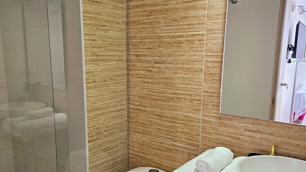 A modern bathroom with a glass shower enclosure, a toilet, a sink with a mirror, and neatly folded towels.
