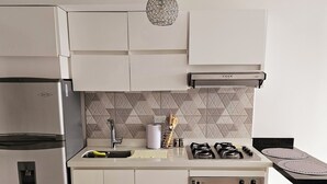A modern kitchen with white cabinetry, a stainless steel refrigerator, a gas stove, and a black oven.