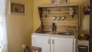 A compact kitchen with a wooden backsplash, a sink, and a small countertop. There are jars, a pitcher, and a basket of fruit on the counter. - Agriturismo Dandelion - Suite Rosmarinus (Citta della Pieve)