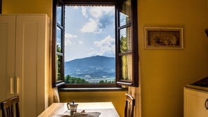 A dining table with a window view of a landscape, a framed picture on the wall, and a cabinet to the right. - Agriturismo Dandelion - Suite Rosmarinus (Citta della Pieve)