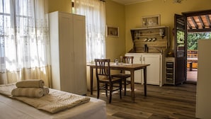 A bedroom with a bed, a wooden table, and a chair. There is a kitchenette with a sink and cabinets. - Agriturismo Dandelion - Suite Rosmarinus (Citta della Pieve)