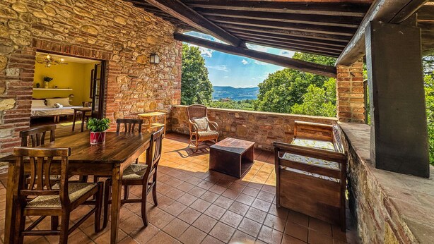 A rustic stone-walled room with a wooden table and chairs, a small sofa, and a view of the landscape. - Agriturismo Dandelion - Suite Rosmarinus (Citta della Pieve)
