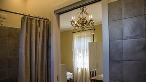 A bathroom with a shower curtain, a chandelier, and a bed in the background. - Agriturismo Dandelion - Suite Rosmarinus (Citta della Pieve)