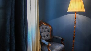 Ein Zimmer mit einer dunkelblauen Wand, einem blau gepolsterten Sessel mit gebogener Rückenlehne und einer hohen Stehlampe mit Holzfuß und beiger Lampenschirm.