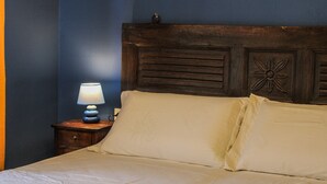Ein Bett mit weißer Bettwäsche, ein hölzerner Kopfseitenverkleidung mit floralen Schnitzereien und eine Nachttischlampe auf einem Holznachttisch.