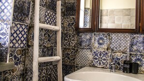 Ein Badezimmer mit einem weißen Waschbecken, einem Spiegel mit Holzrahmen und einer gefliesten Wand mit blau-weißen Mustern.