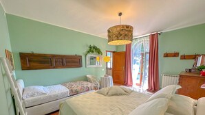 A bedroom with two single beds, a wooden headboard, a small table with a lamp, a chair, and a window with curtains.