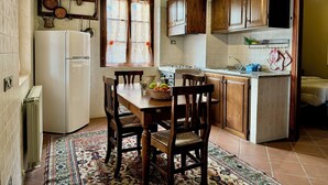 A compact kitchen with a dining area, featuring wooden cabinets, a white refrigerator, and a patterned rug. - Agriturismo Dandelion - Casetta Pane e Burro (Citta della Pieve)