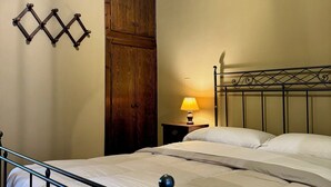 A bedroom with a bed, wooden wardrobe, nightstand with lamp, and decorative wall piece. - Agriturismo Dandelion - Casetta Pane e Burro (Citta della Pieve)