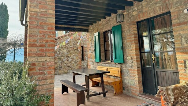 A rustic outdoor seating area with a wooden table and bench, stone walls, and a door with green shutters. - Agriturismo Dandelion - Casetta Pane e Burro (Citta della Pieve)