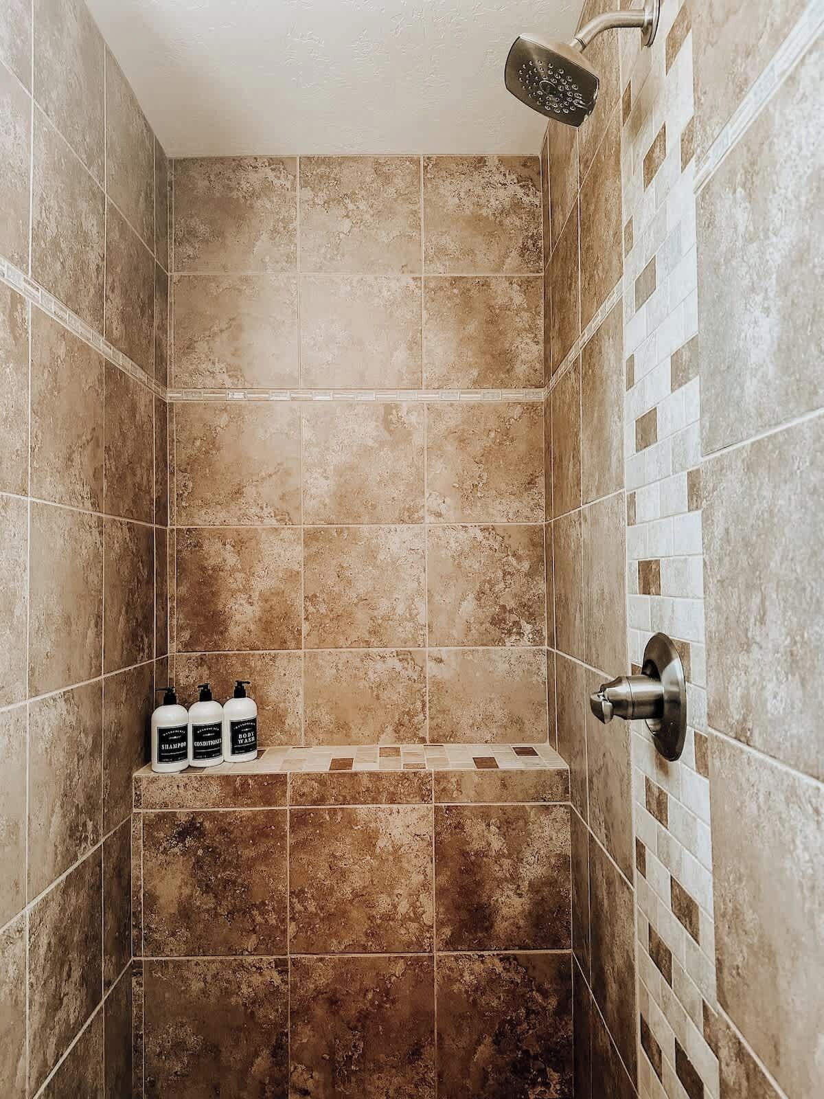 Een douche met beige tegels, een douchekop en een plank met toiletartikelen.