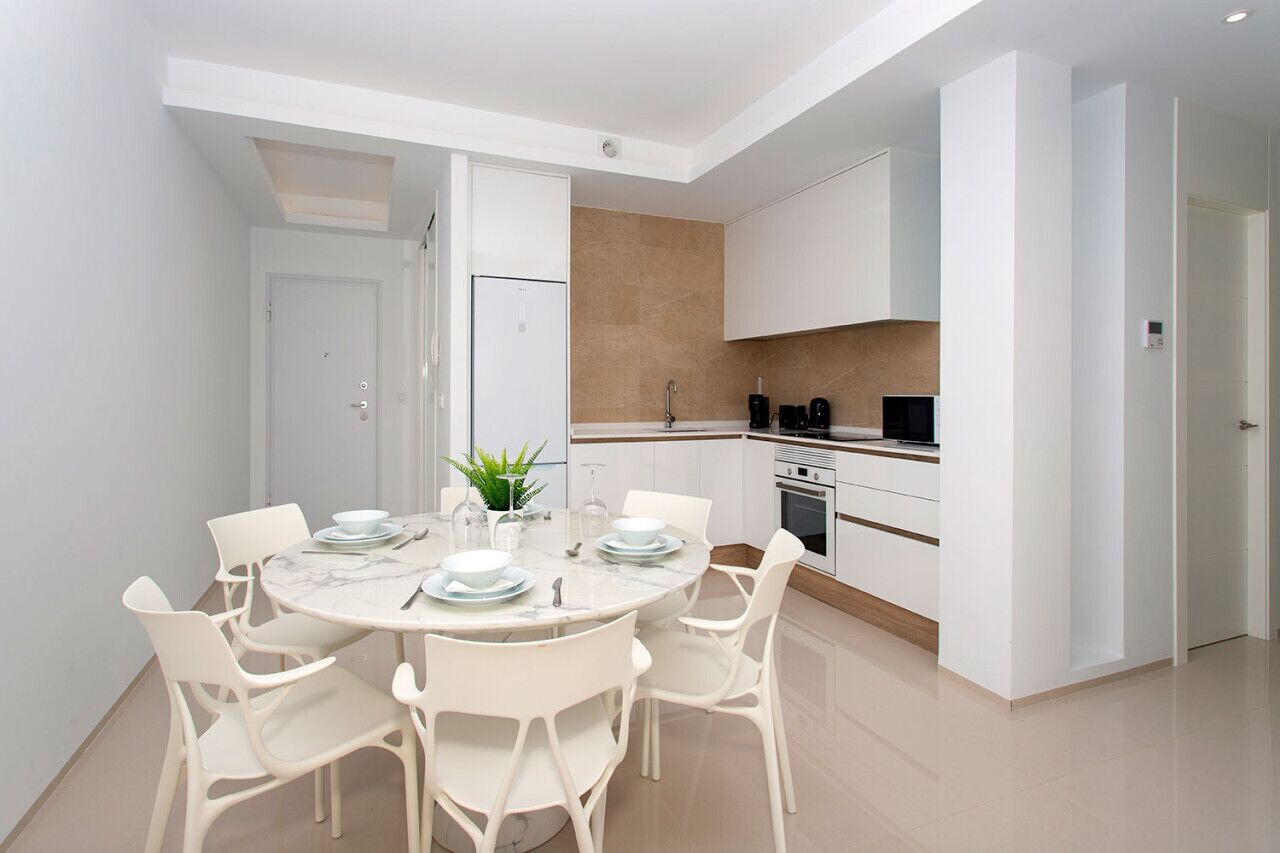 Una cocina moderna con muebles blancos, horno empotrado y cafetera.