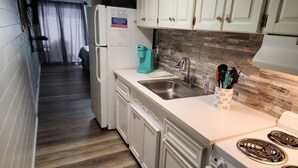 A compact kitchen with white cabinets, a stainless steel sink, a coffee maker, and a stove. - Ambassador 128- Gulf Front - Pet Friendly (Panama City Beach)